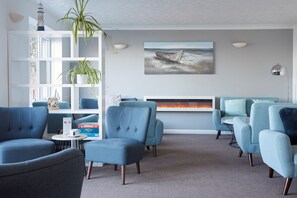 A modern living room with blue armchairs, a white fireplace, and a nautical-themed painting.