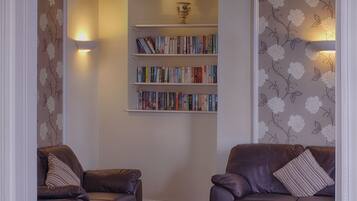 A room with two leather armchairs, a bookshelf with books, and floral wallpaper.
