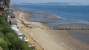 A coastal beach with a row of boats, a promenade, and a clear view of the sea and distant cliffs. - Luccombe Manor Country House Hotel (Shanklin)