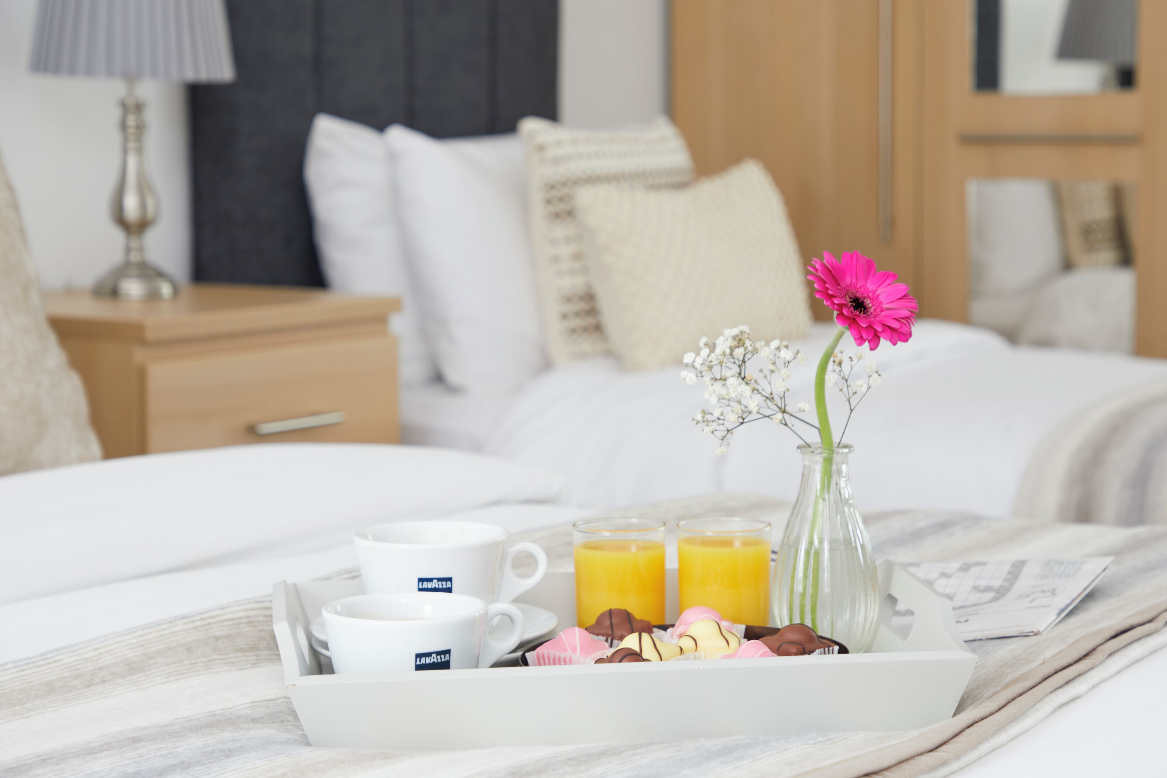 A neatly made breakfast tray with coffee cups, juice glasses, and pastries on a bed in a hotel room.