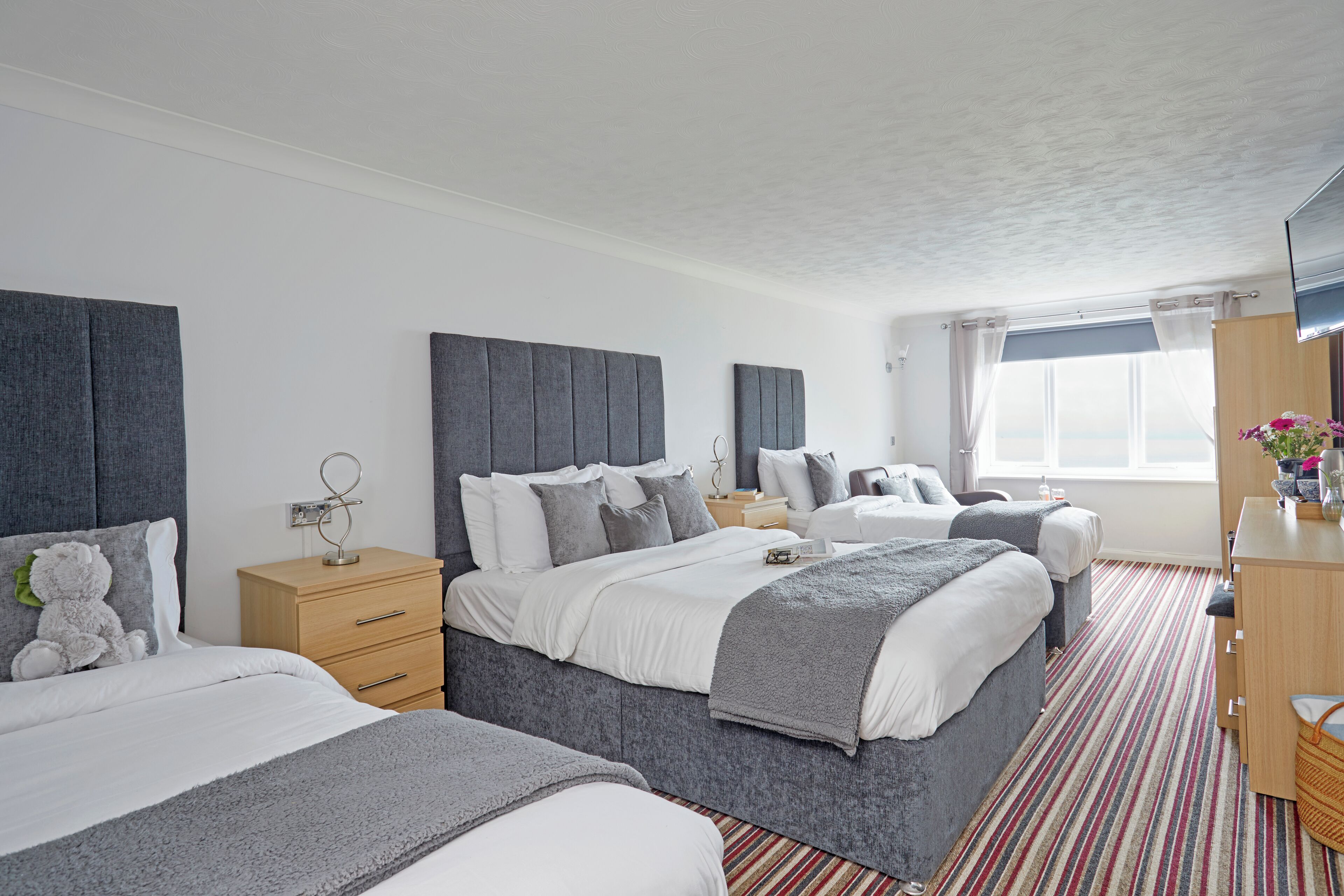 A hotel room with two beds, a wooden dresser, a TV, and a window with curtains.