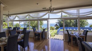 A dining area with large windows, wooden flooring, and a view of the sea. - Luccombe Manor Country House Hotel (Shanklin)