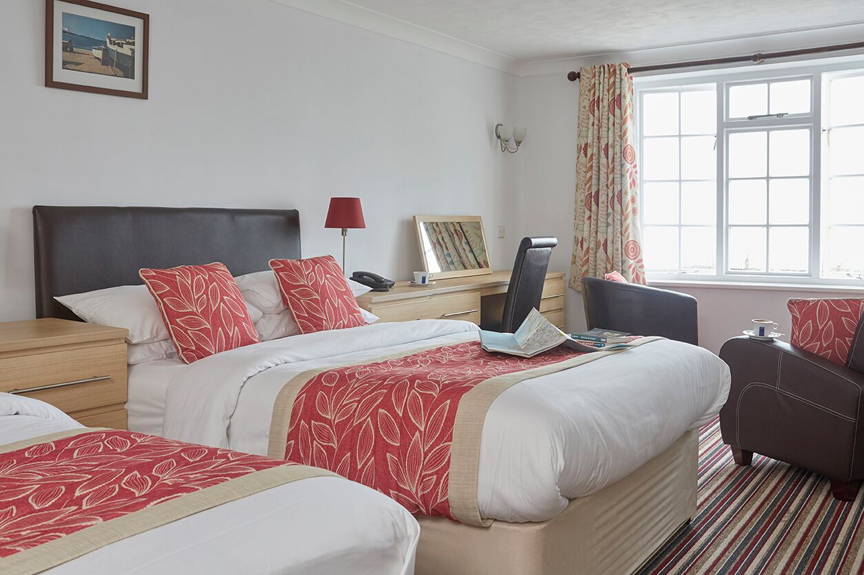 Una habitación de hotel con una cama grande, un escritorio con lámpara, una silla y un ventanal con cortinas.
