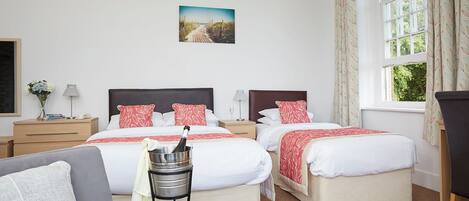 A hotel room with two beds, a sofa, a nightstand, a lamp, a picture on the wall, and a window with curtains.