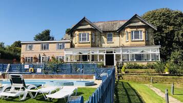 Traditional building with a spacious conservatory and adjacent pool area surrounded by lush greenery.