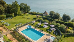 A pool area with lounge chairs and umbrellas, surrounded by well-maintained lawns and a view of the sea. - Luccombe Manor Country House Hotel (Shanklin)