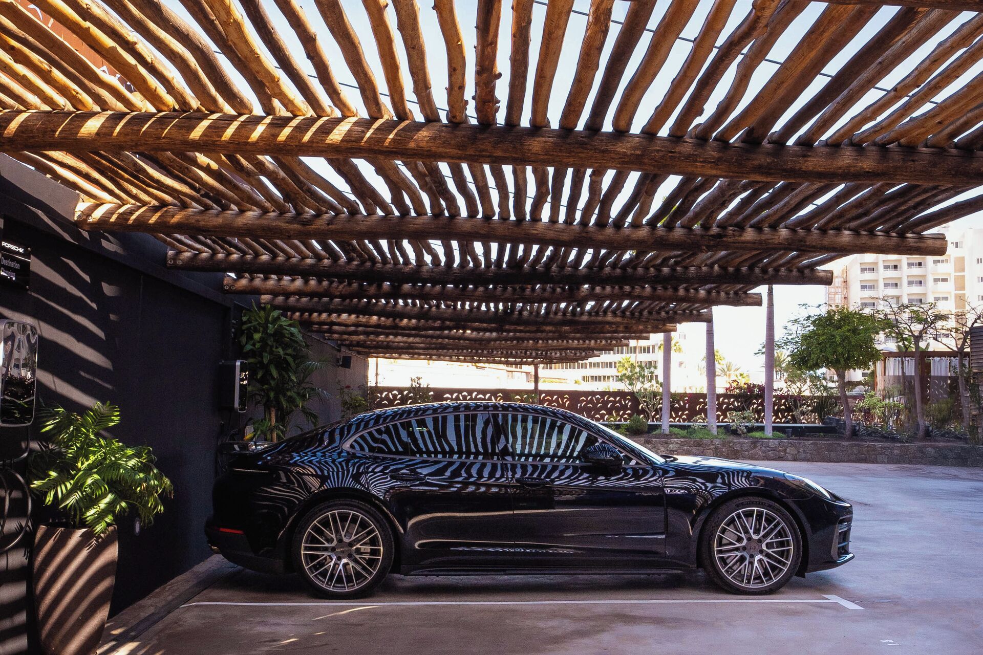 A black car parked under a wooden pergola structure.
