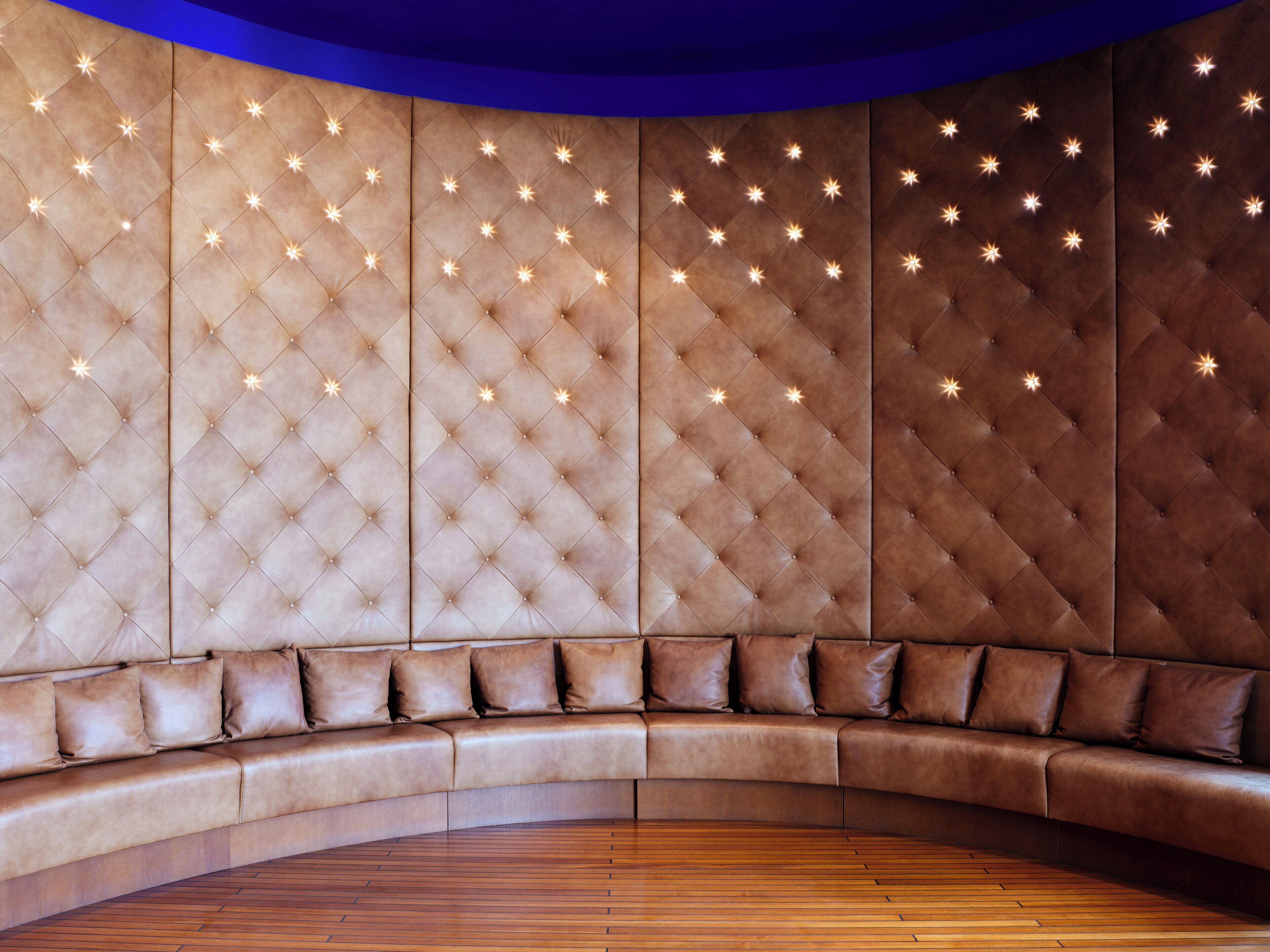 A curved sofa with a tufted backrest and a wooden floor.