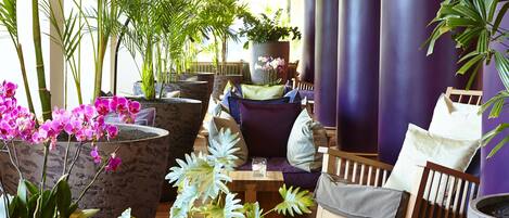 A lounge area with a sofa, chairs, and a coffee table, surrounded by potted plants and orchids.