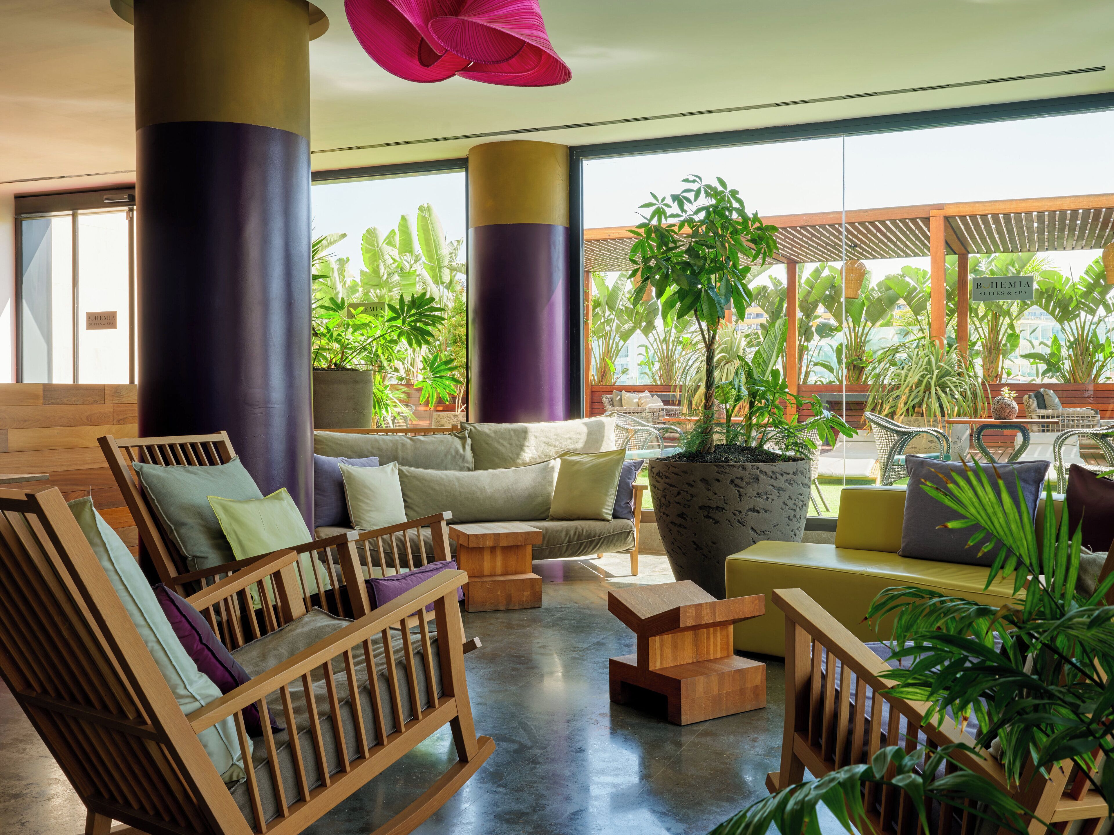 A spacious indoor area with wooden furniture, a large potted plant, and a view of lush greenery outside.