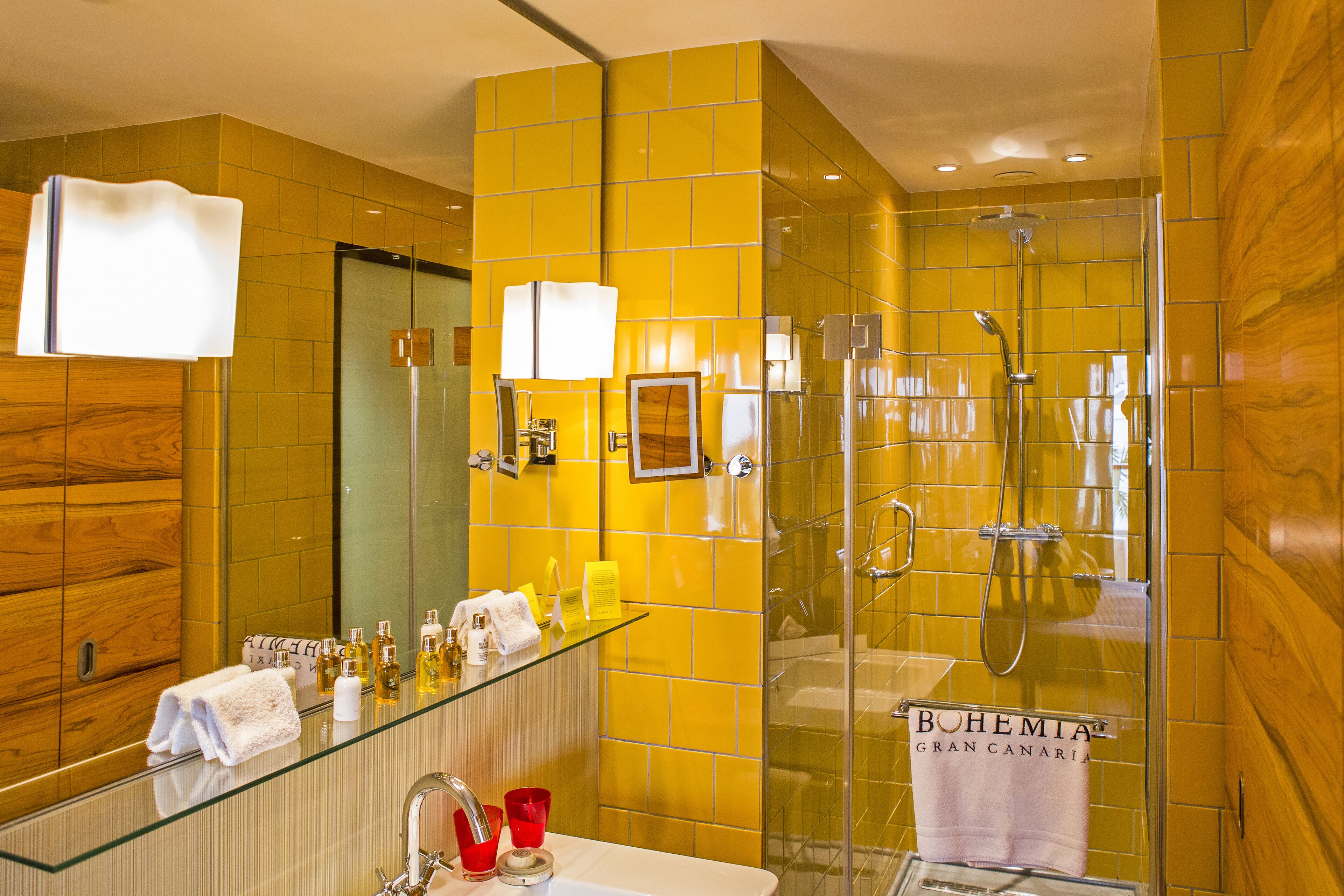 A modern bathroom with a glass shower enclosure, a large mirror, and a glass-topped vanity.