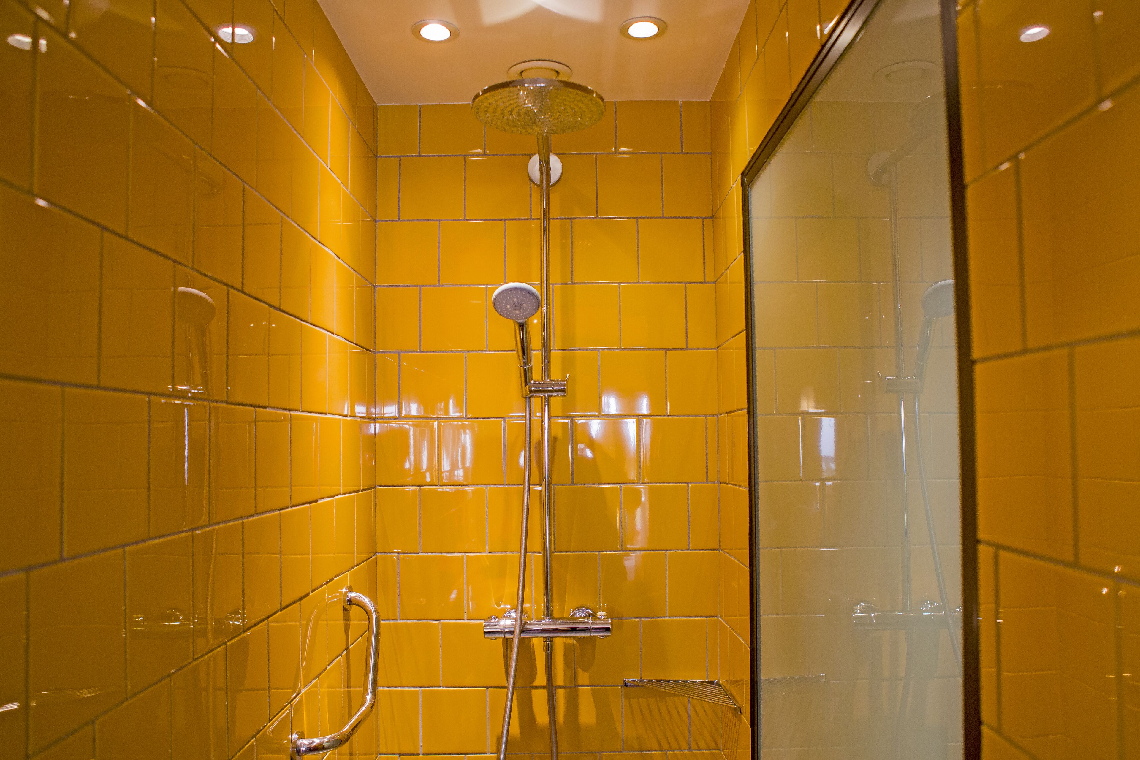 Ducha con azulejos amarillos, puerta de vidrio y cabezal de ducha manual.