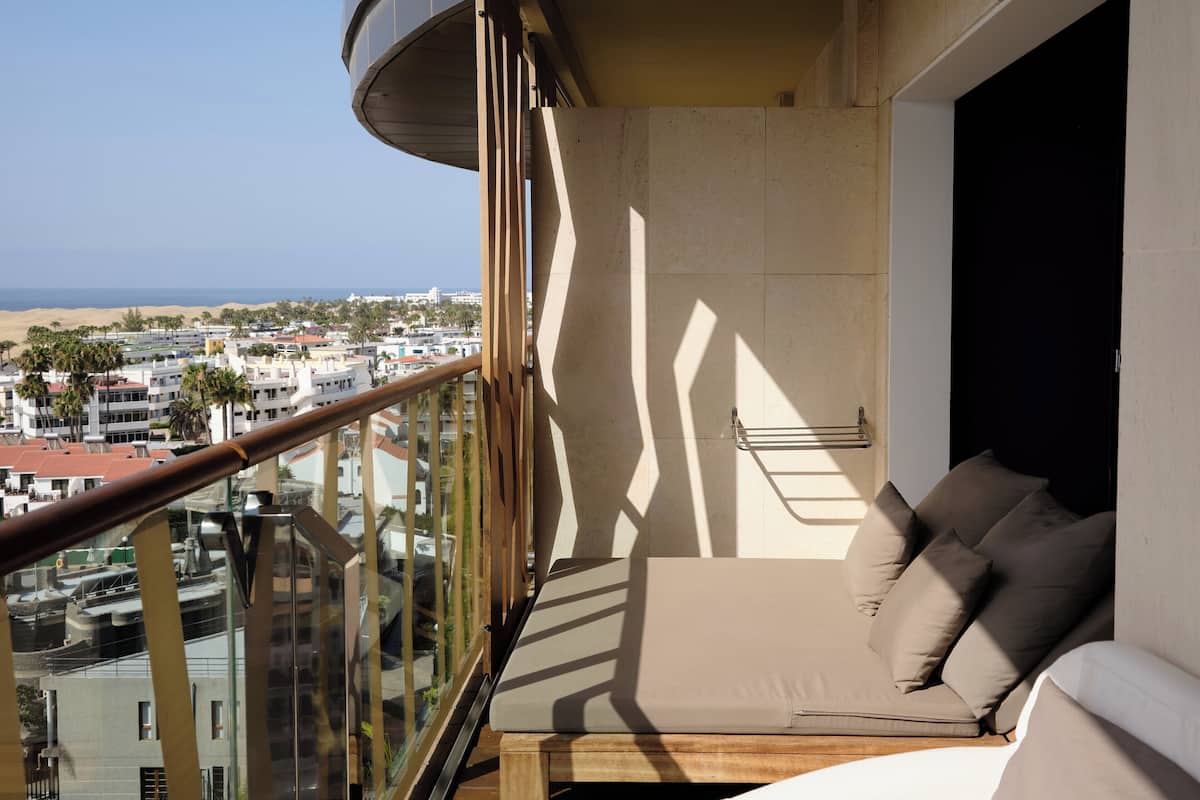 A balcony with a sofa and a towel rack, overlooking a cityscape and the sea.