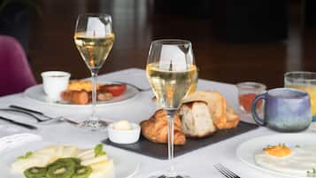 A dining table with a croissant, a glass of white wine, and plates of food including kiwi slices and a poached egg.
