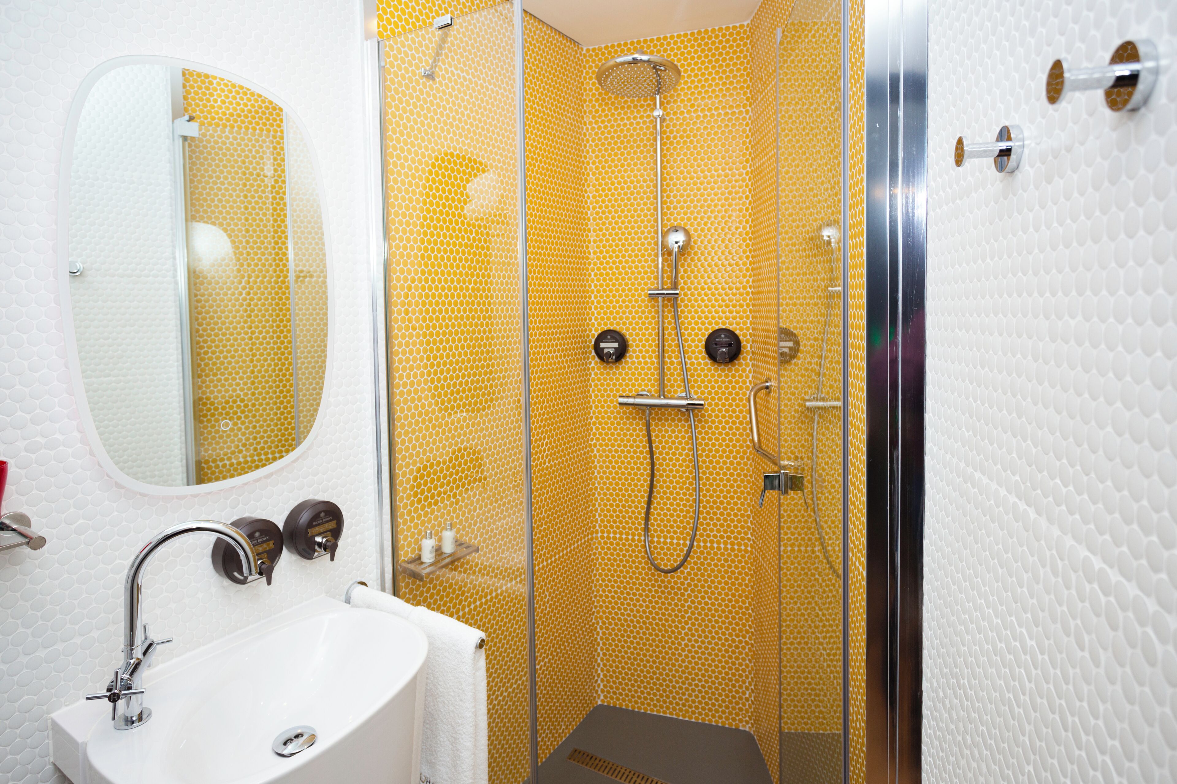 Un bany amb un lavabo blanc, un mirall i una dutxa amb parets de color grog i amb dibuixos.