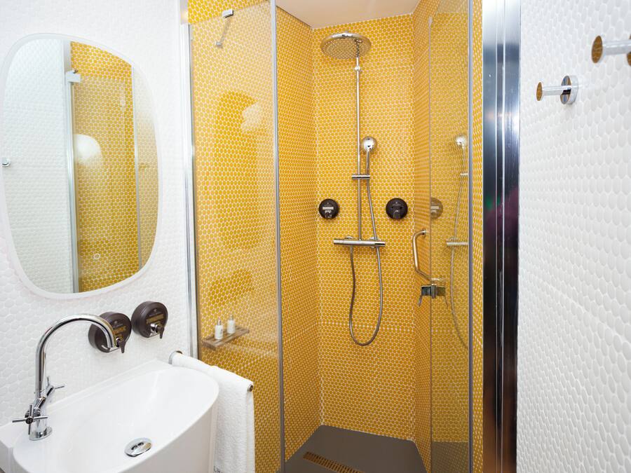 Un baño con lavamanos blanco, un espejo y una ducha con paredes de color amarillo con diseño.