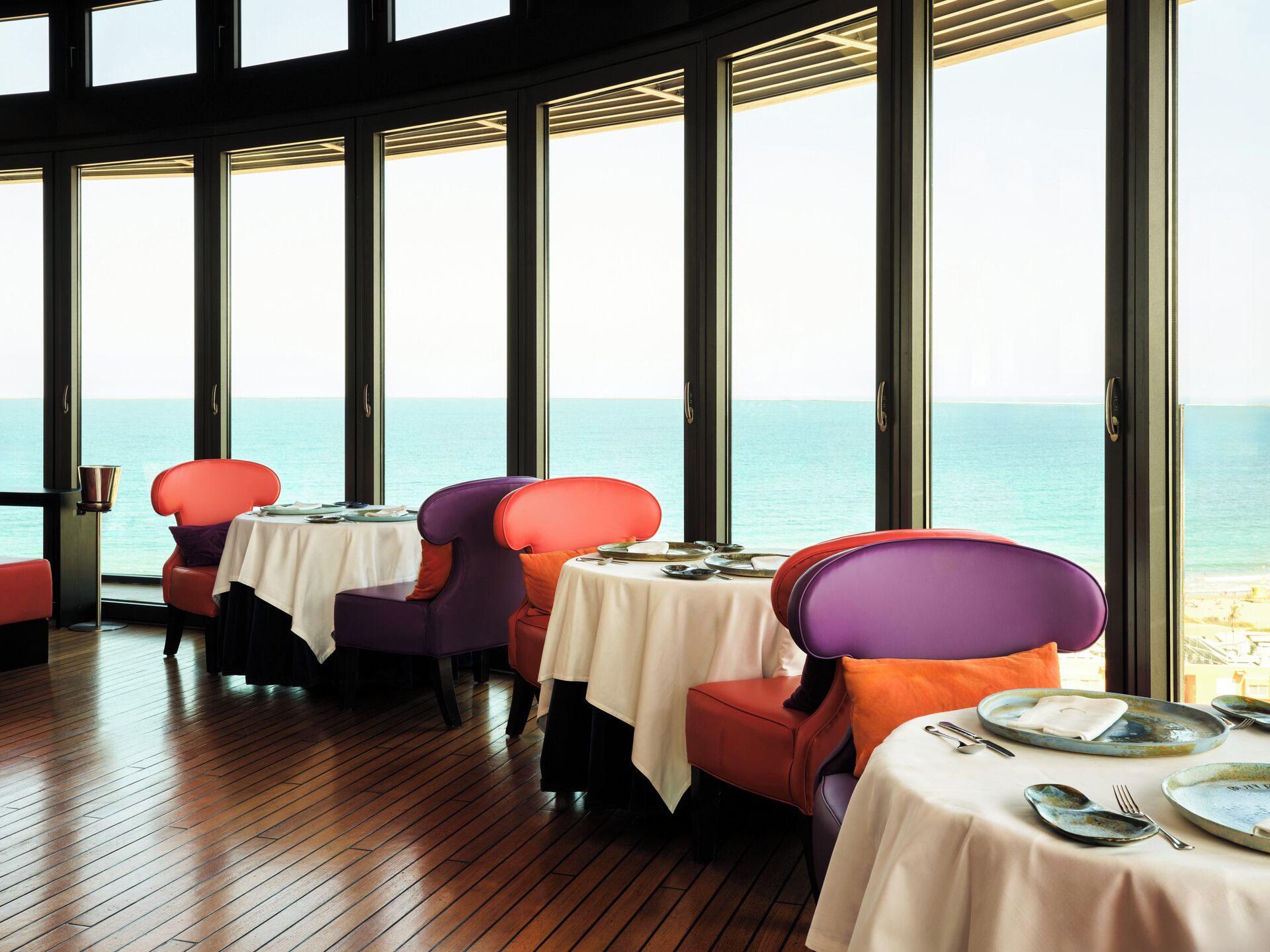 A dining area with large windows, wooden flooring, and tables set for dining.