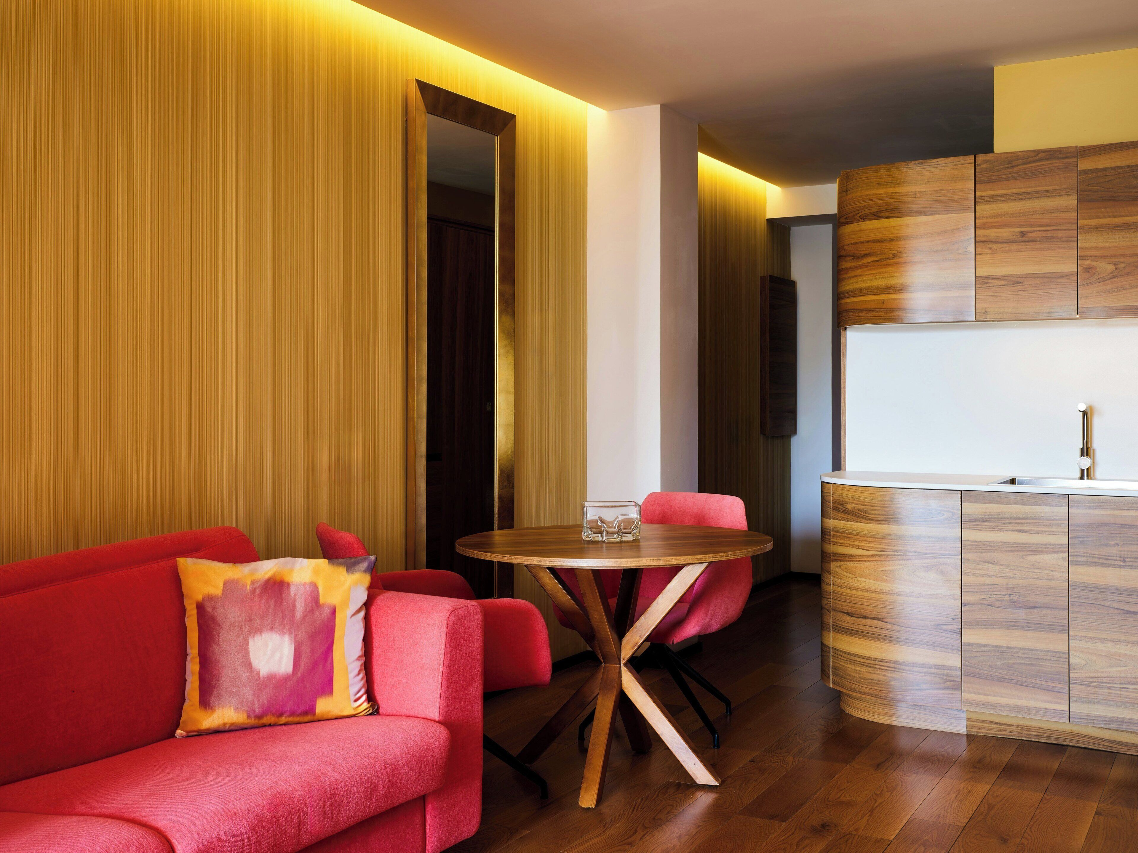 Um interior moderno com um sofá vermelho, uma mesa de madeira redonda e uma área de cozinha com armários de madeira.