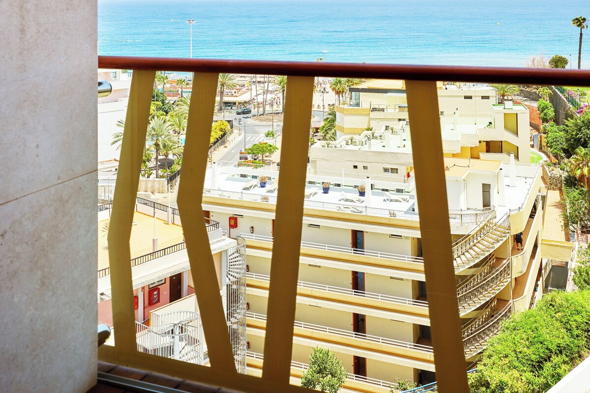 Un balcón con vista al mar y un edificio de varios pisos con balcones.