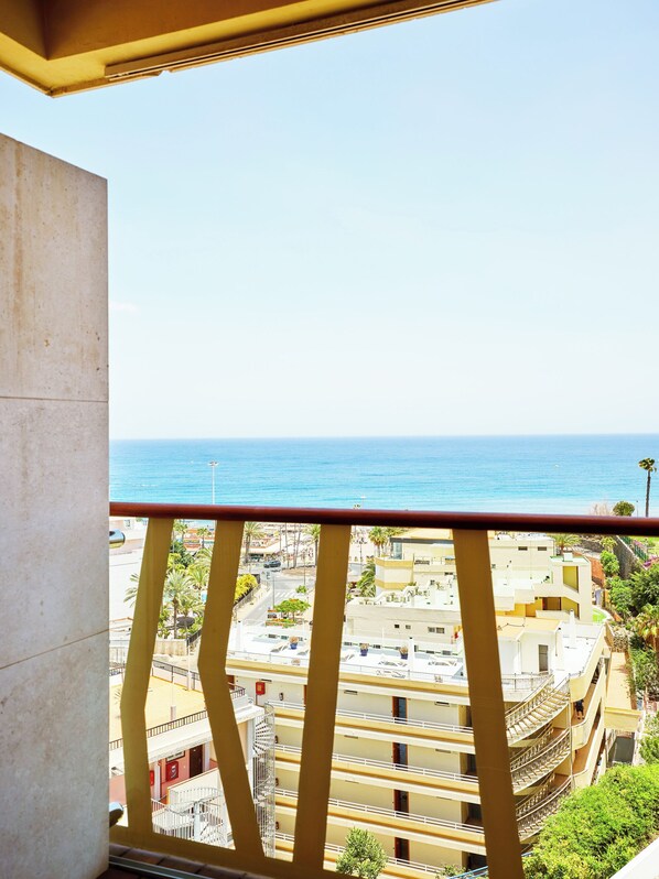Un balcón con vista al mar y un edificio de varios pisos con balcones.