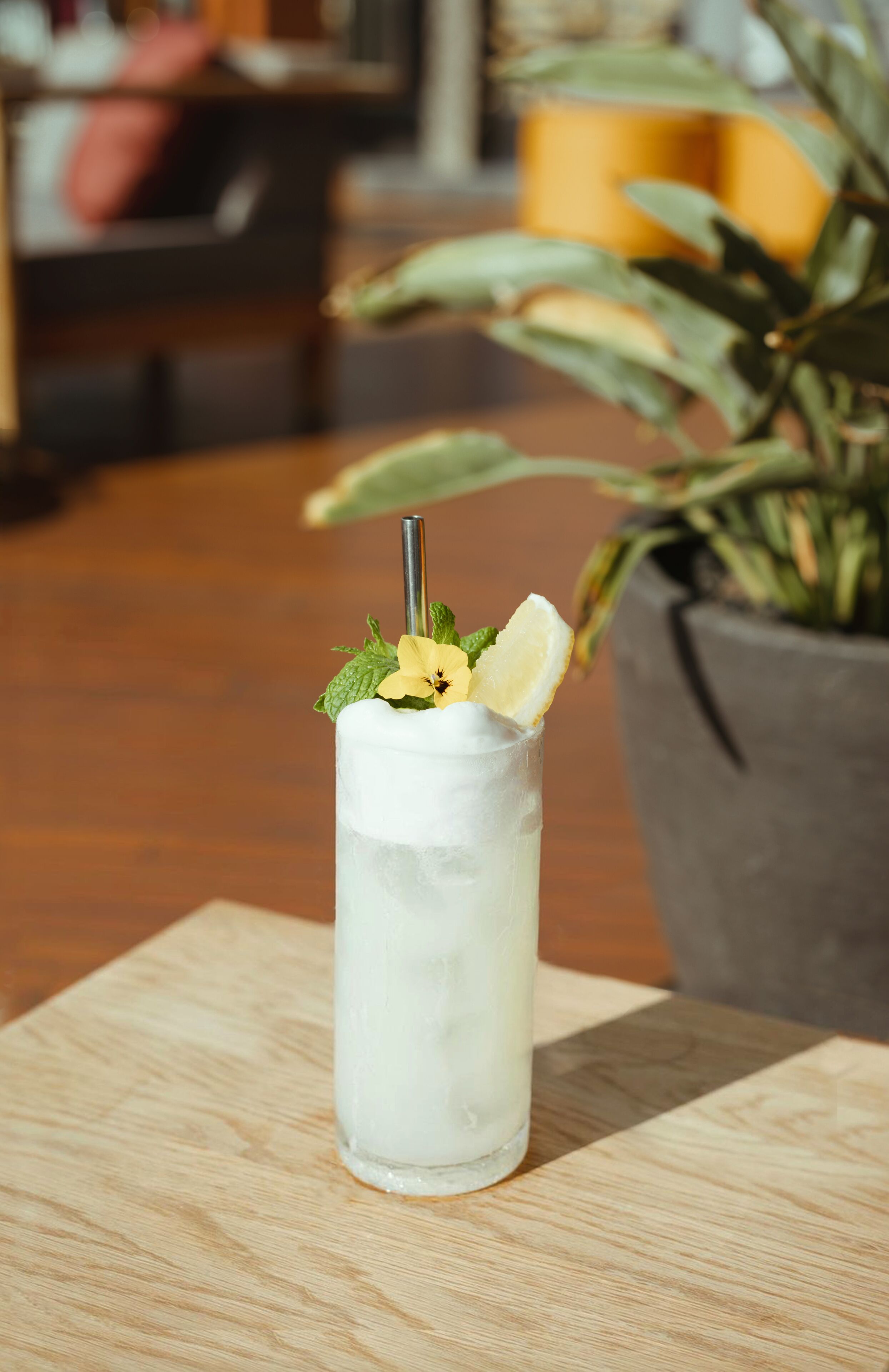 A tall glass with a straw, mint leaves, and a slice of lemon on a wooden table.