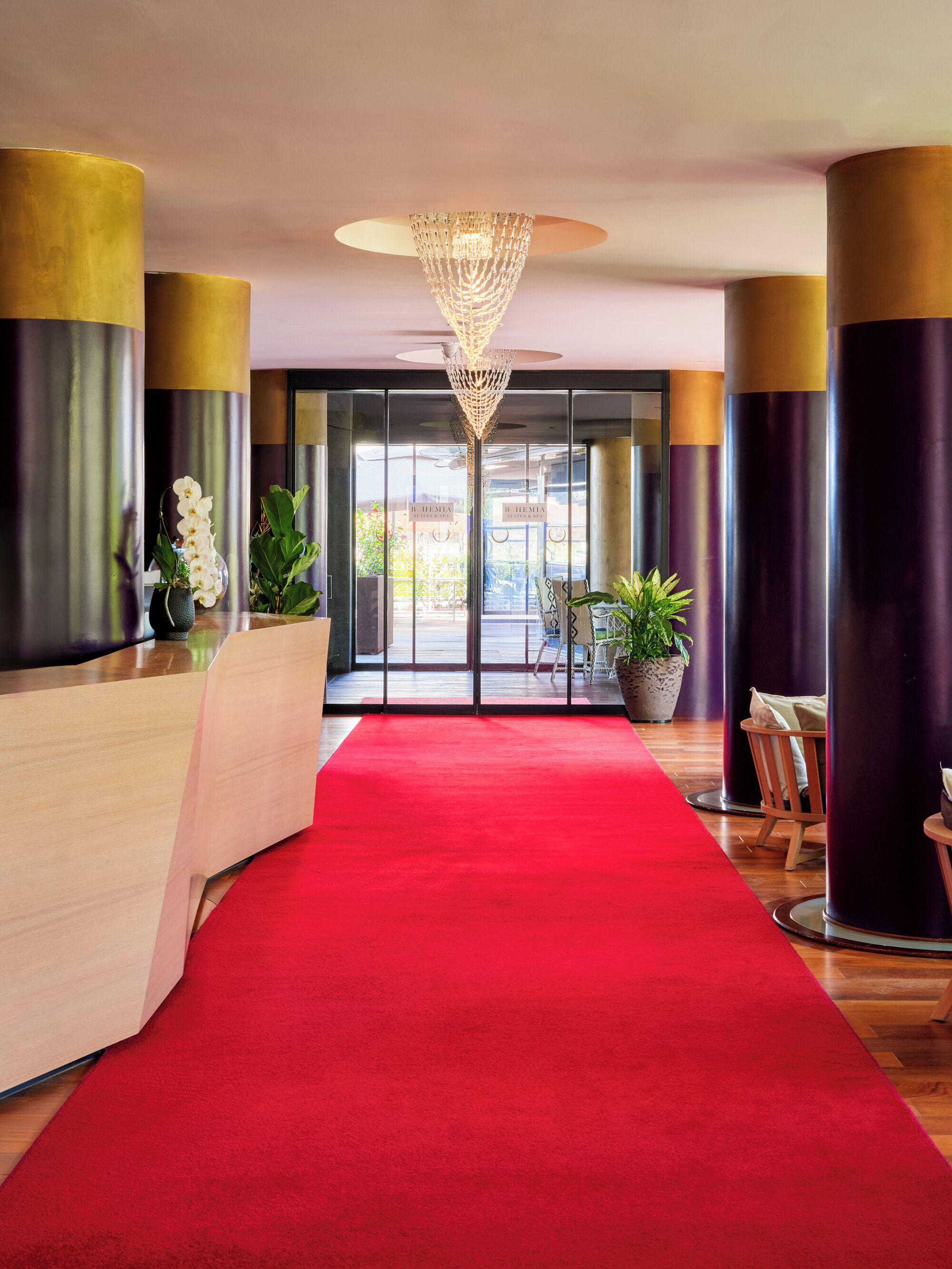 A hotel reception area with a red carpet, a modern chandelier, and a reception desk.