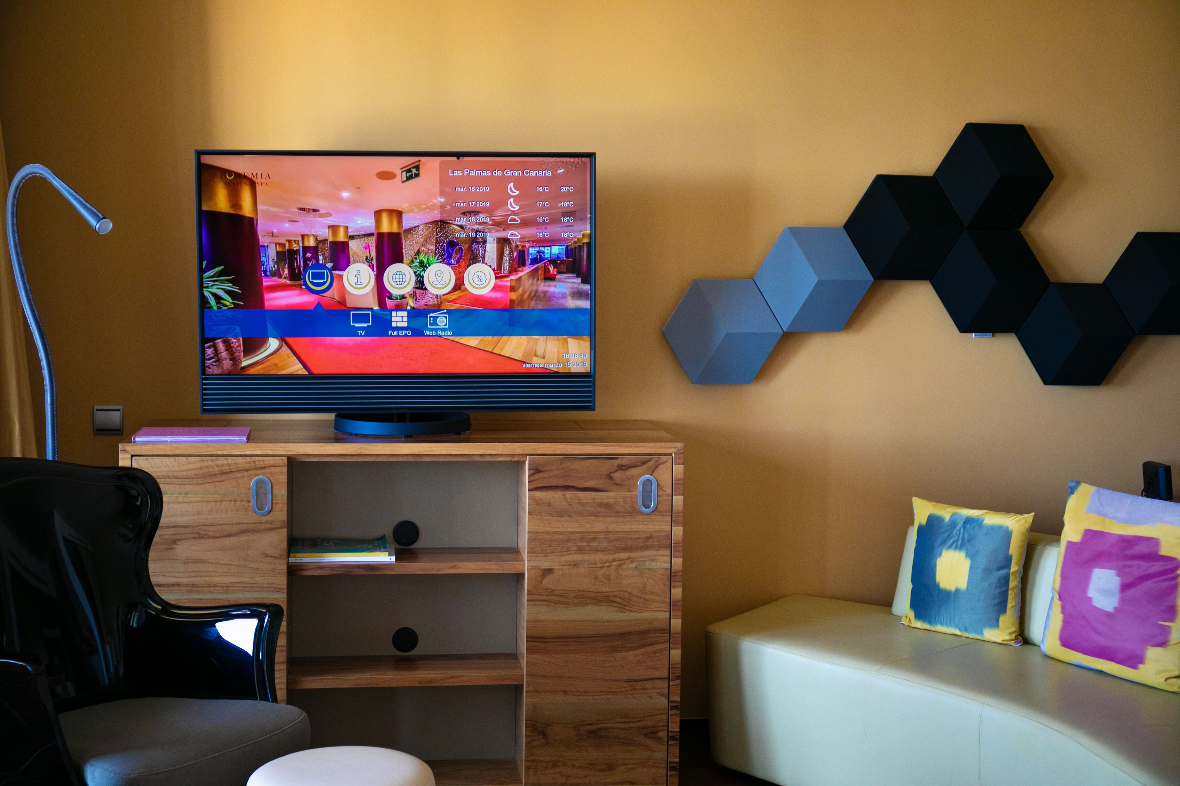A modern living room with a flat-screen TV, wooden entertainment unit, and a sofa with colorful cushions.