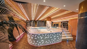 A luxurious indoor pool area with a modern design, featuring a central hot tub surrounded by a wooden floor and a unique ceiling light fixture. - Bohemia Suites & Spa - Adults only (San Bartolomé de Tirajana)