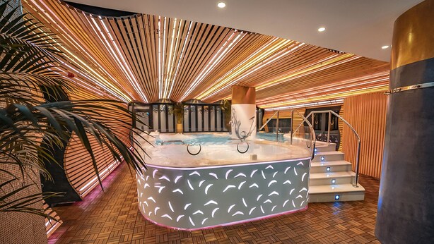 A luxurious indoor pool area with a modern design, featuring a central hot tub surrounded by a wooden floor and a unique ceiling light fixture. - Bohemia Suites & Spa - Adults only (San Bartolomé de Tirajana)