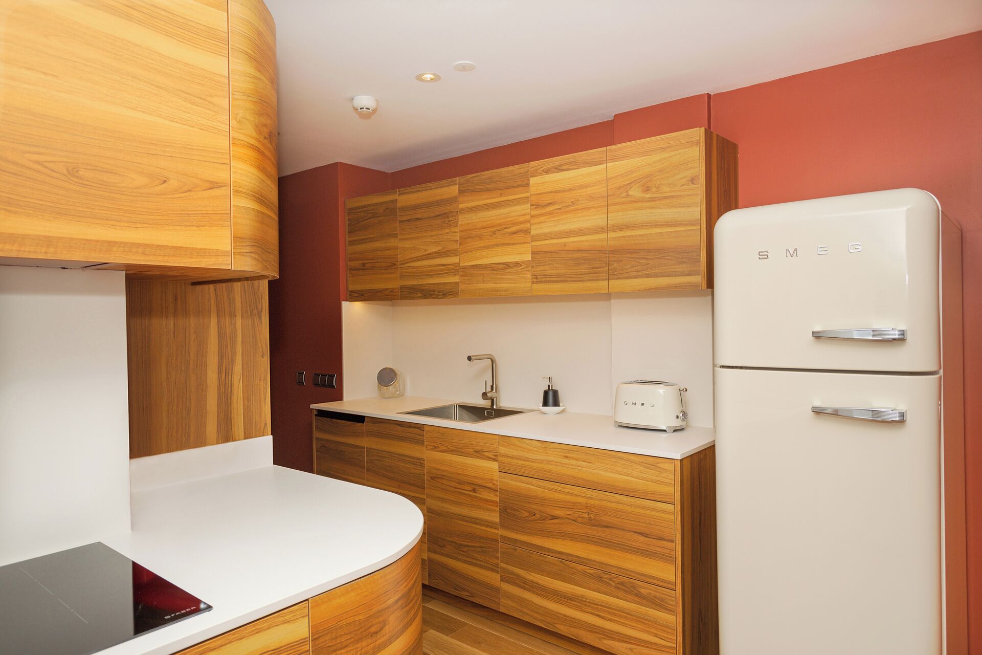 Una cocina compacta con armarios de madera, una encimera blanca, un fregadero, un tostador y un refrigerador blanco.