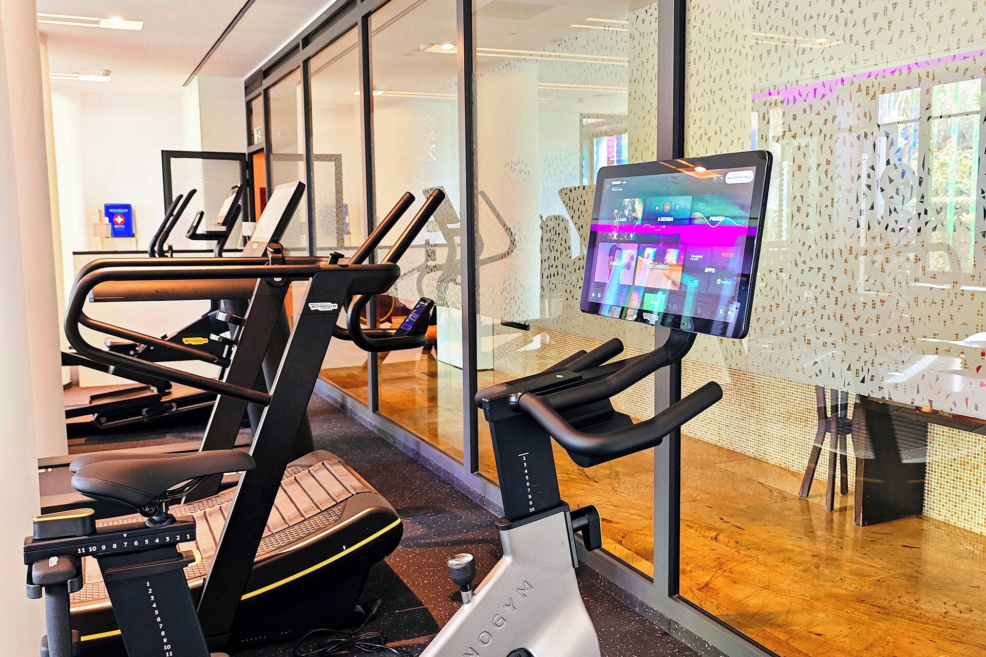 Un gimnasio con equipo de ejercicio, una pantalla digital y una pared con diseño.