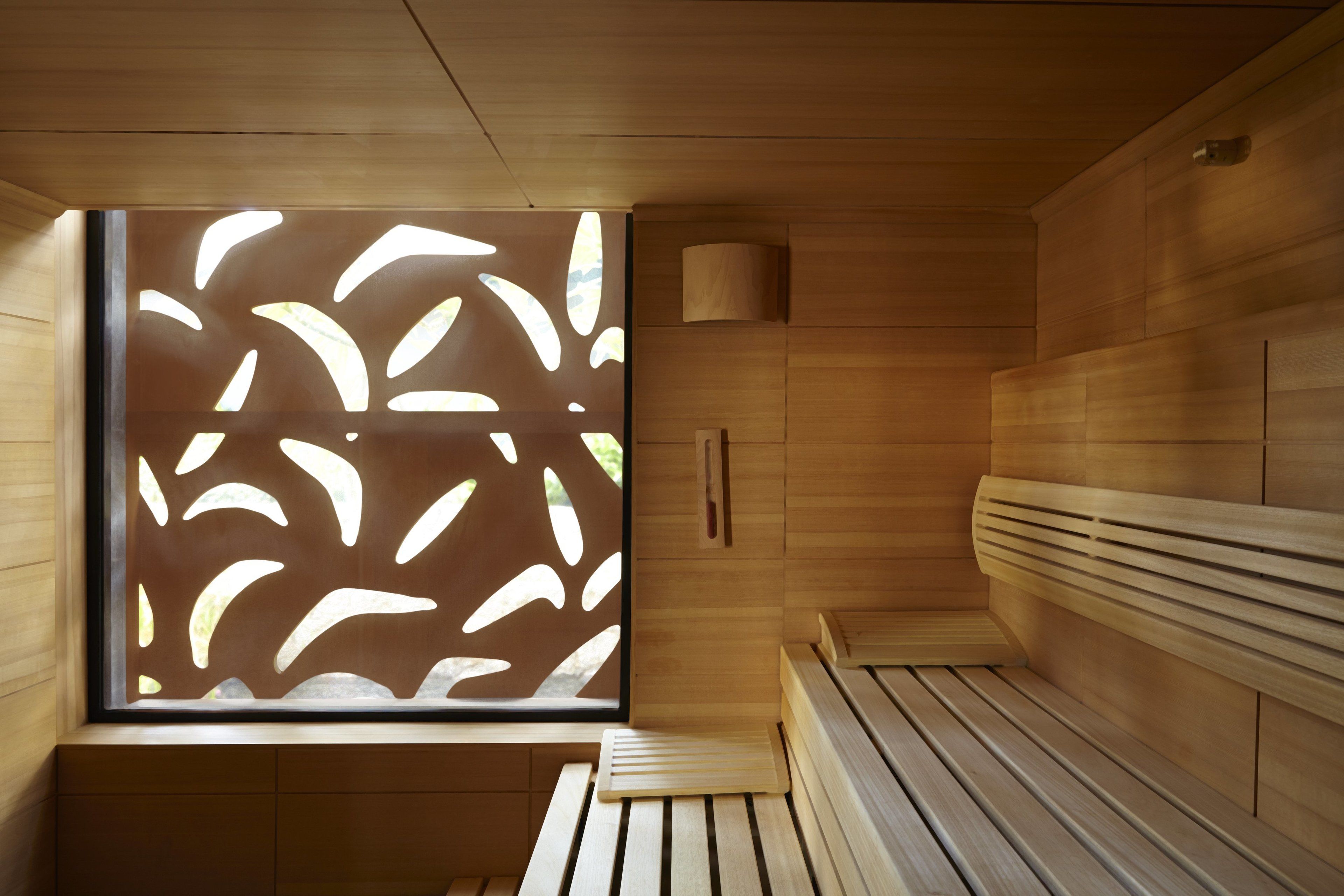 A sauna room with wooden benches and a large window with a leaf pattern.