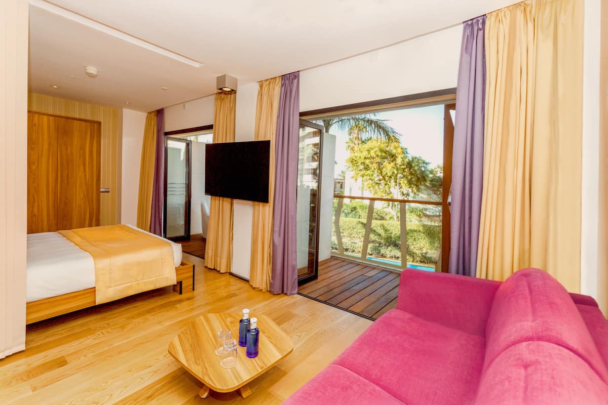 A hotel room with a bed, a sofa, a TV, and a balcony with curtains.