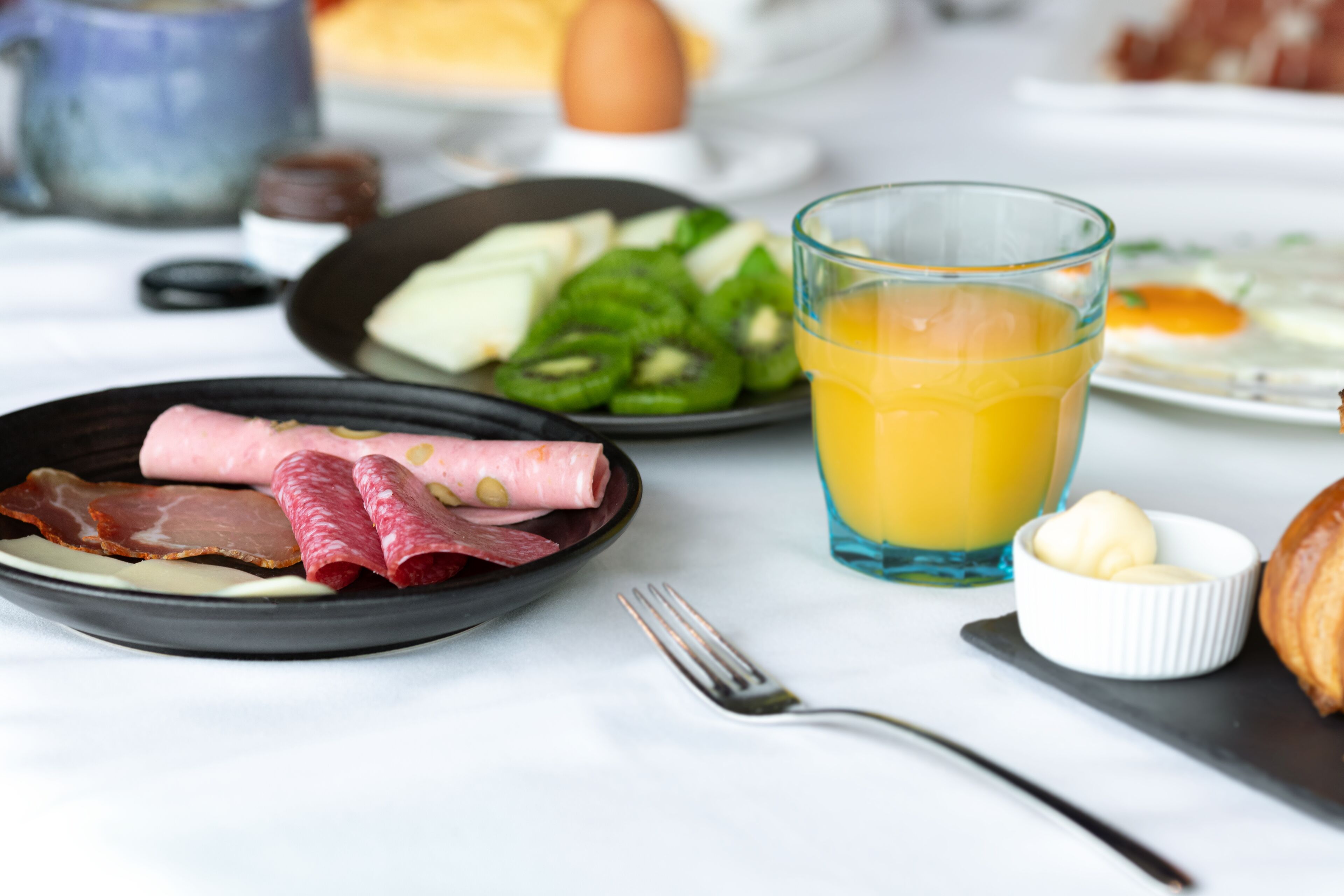 A breakfast setting with plates of food, a glass of orange juice, and a fork on a table.