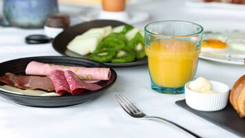 Desayuno servido con platos de comida, un vaso de jugo de naranja y un tenedor sobre la mesa.