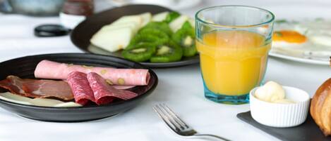 A breakfast setting with plates of food, a glass of orange juice, and a fork on a table.