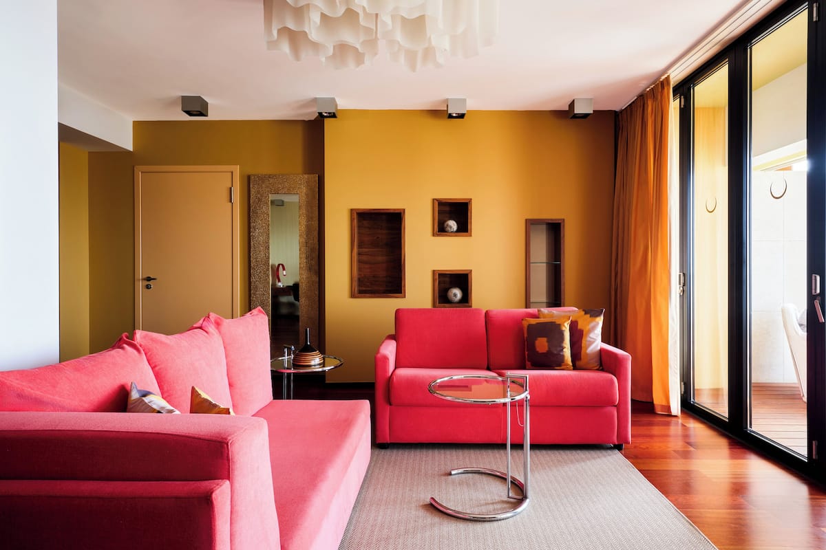 A modern living room with a red sofa, a glass coffee table, and a yellow accent wall.