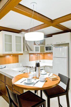 A modern kitchen with white cabinetry, a round dining table, and a hanging light fixture.