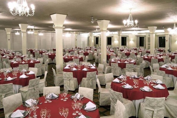 Une salle de banquet avec des tables rondes dressées pour le repas, chacune étant agrémentée de chaises blanches et de nappes rouges.