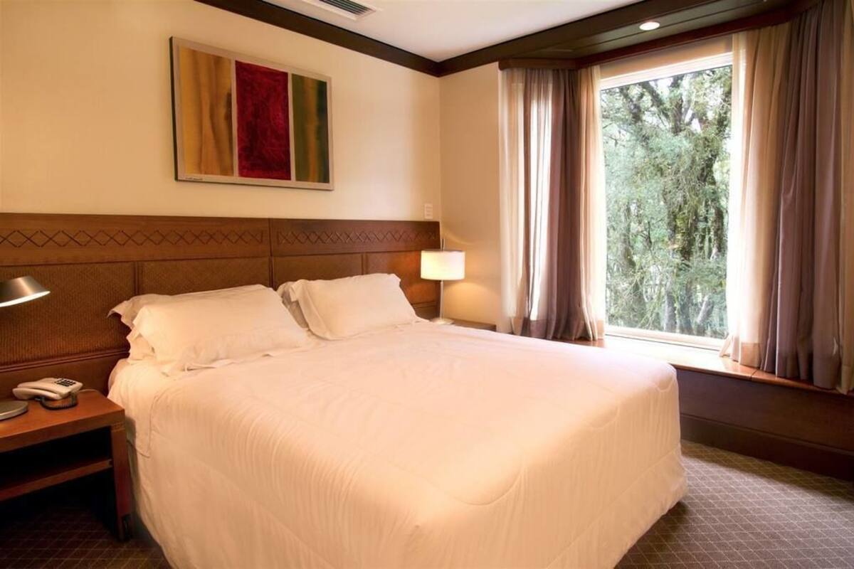 A hotel room with a large bed, a nightstand with a phone, a lamp, and a window with curtains.