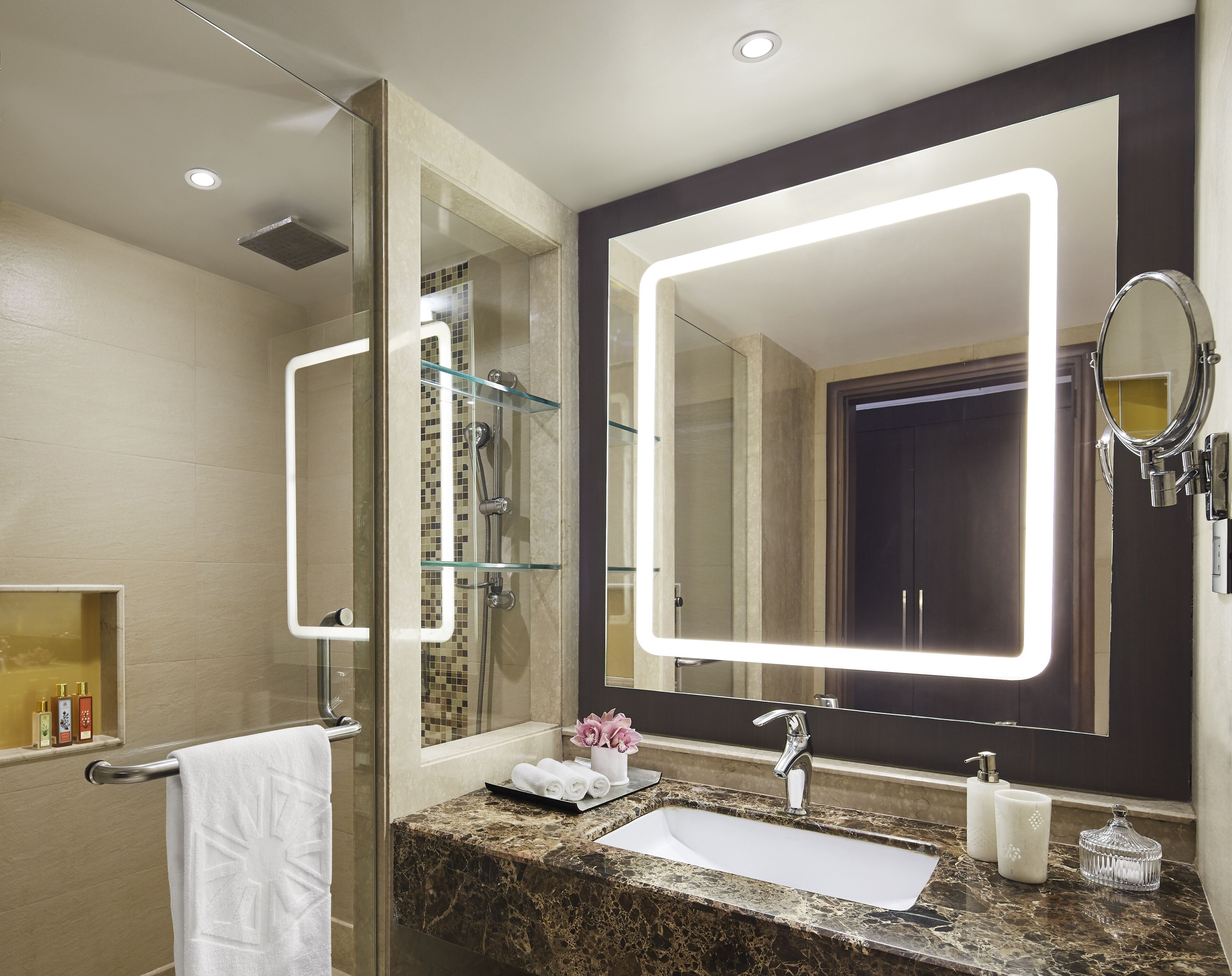 A modern bathroom with a glass-enclosed shower, a marble sink, and a large mirror with integrated lighting.