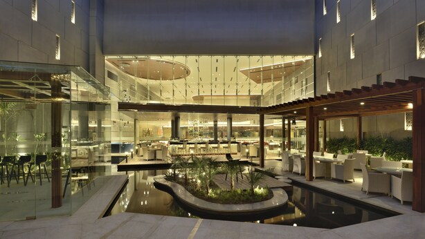 Un atrium intérieur moderne doté d’un élément aquatique central, de murs en verre et d’espaces aménagés pour s’asseoir.