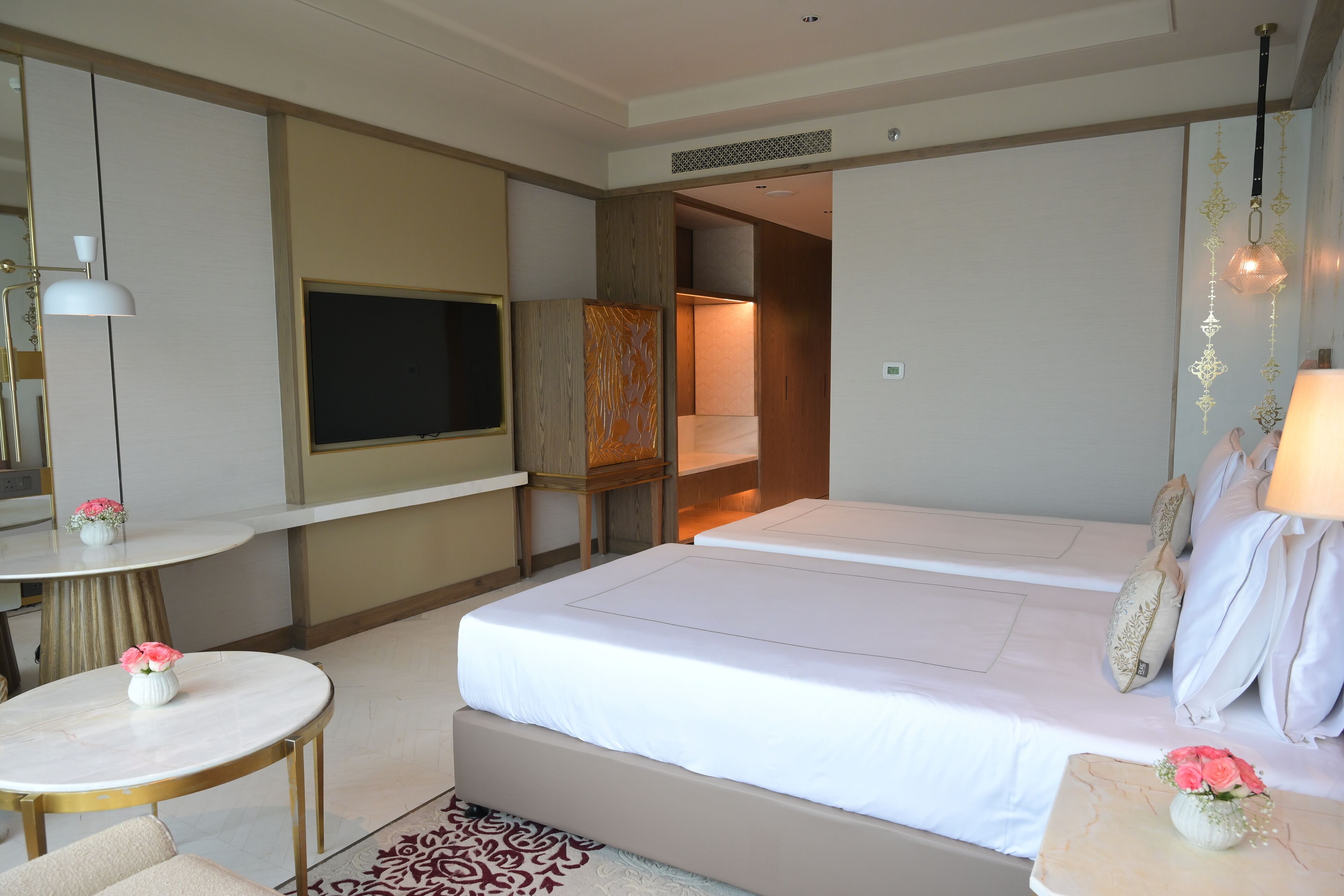 Quarto de hotel com uma cama, televisão, secretária e uma pequena mesa com flores.