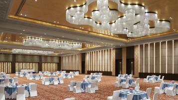 Un salón de banquetes con mesas redondas, sillas blancas y manteles azules.