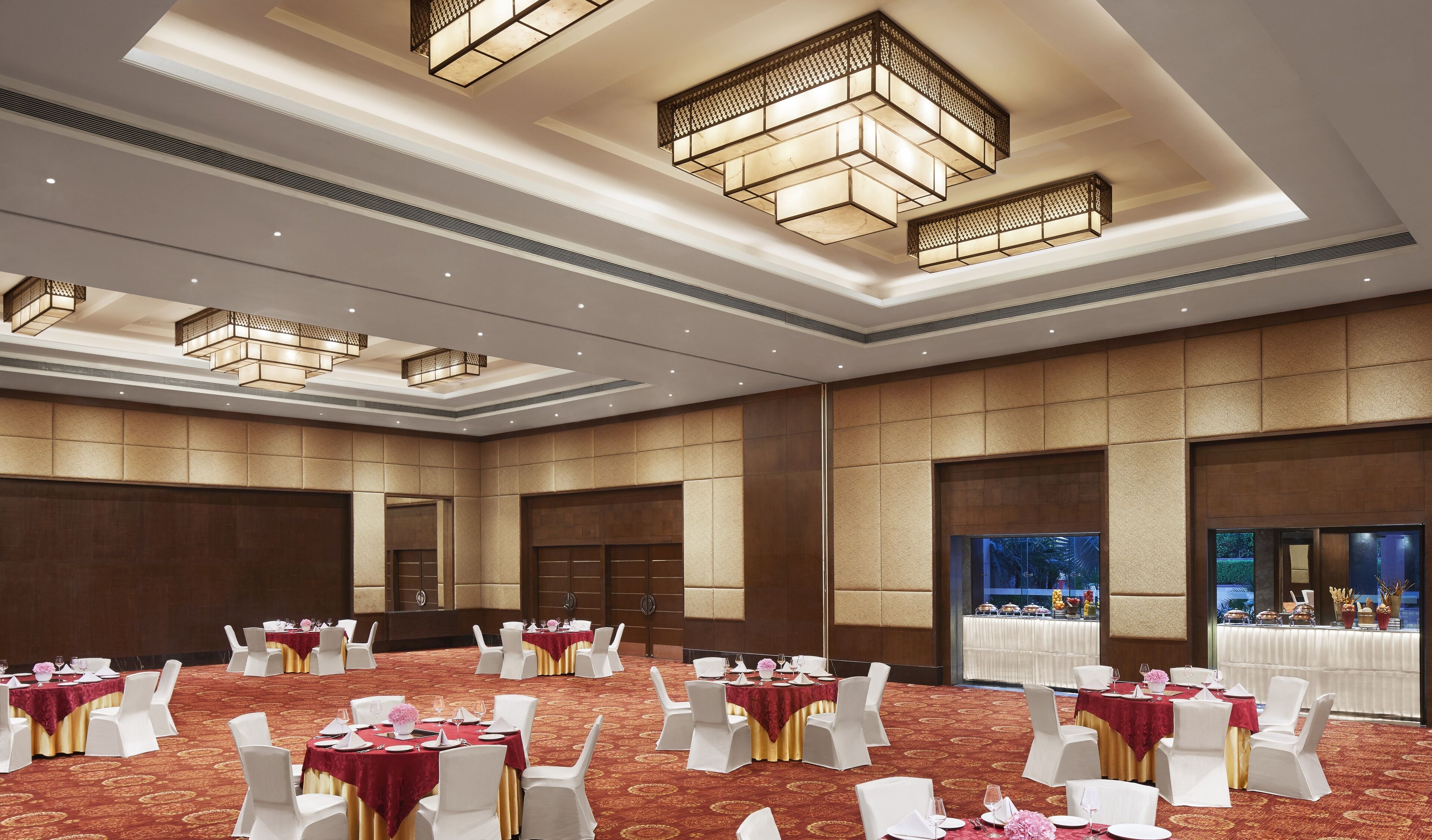 A banquet hall with round tables, white chairs, and red tablecloths.