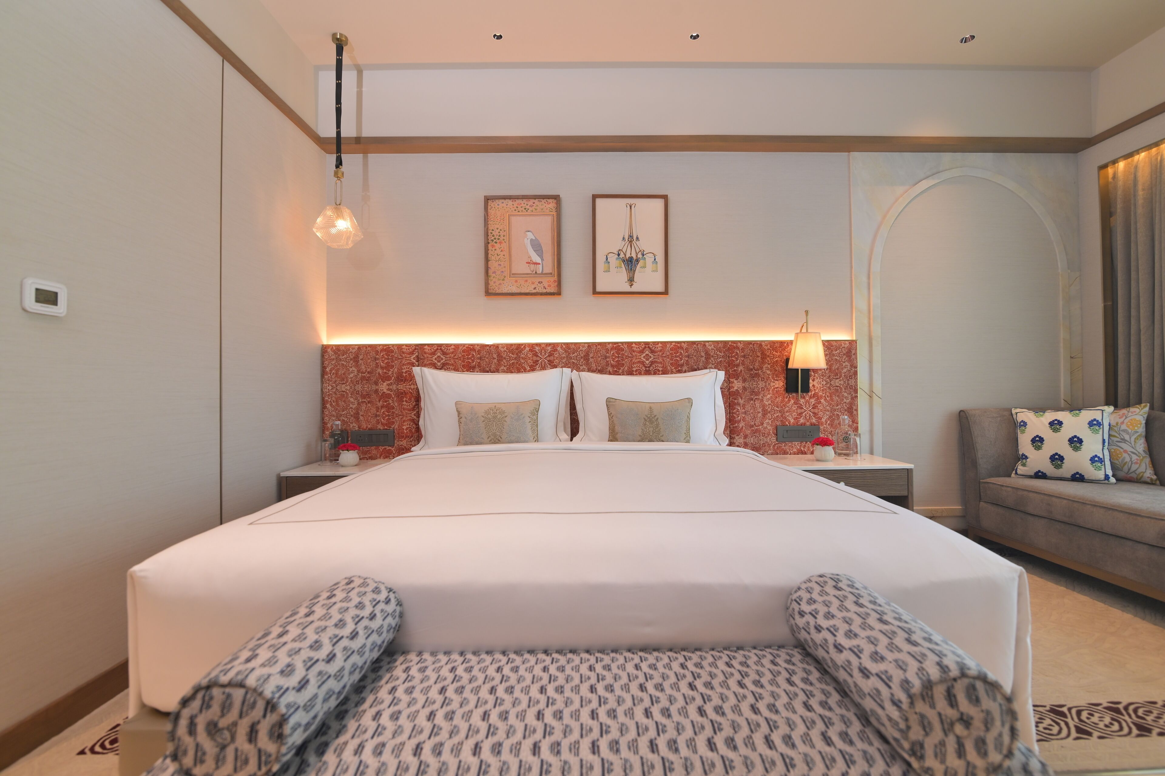 A hotel room with a large bed, two bedside tables, a sofa, and a patterned rug.