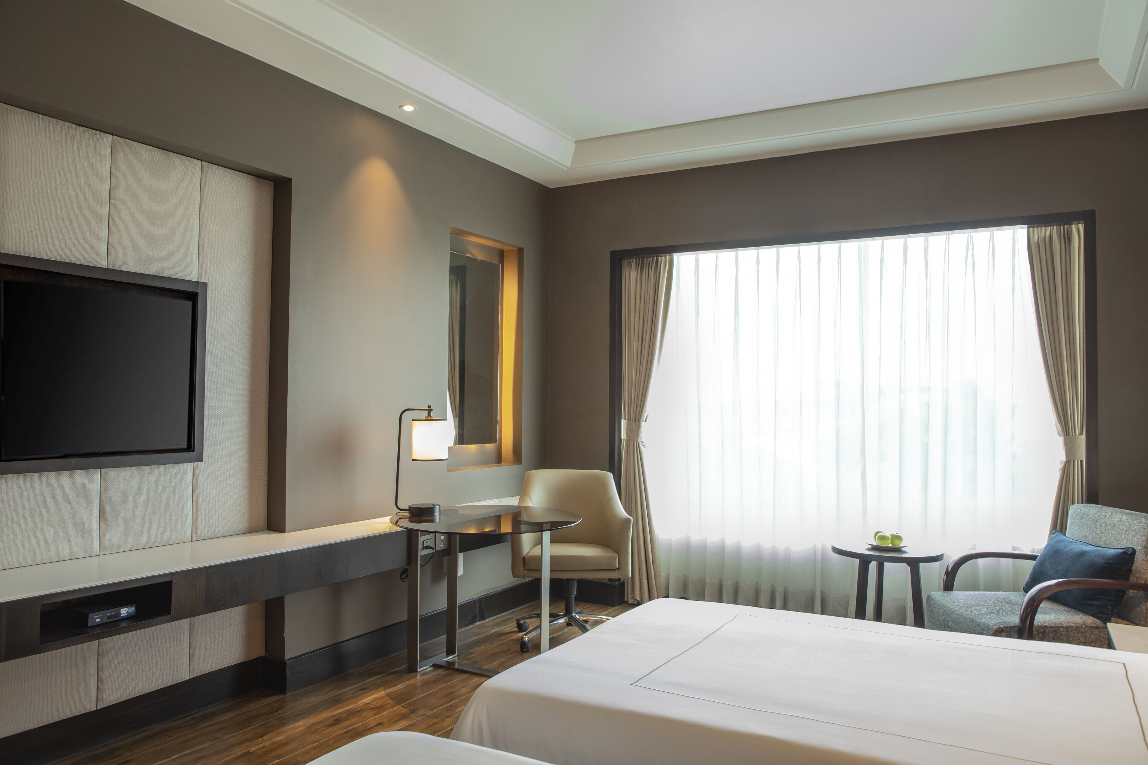 A hotel room with a bed, a desk, a chair, a TV, and a window with curtains.