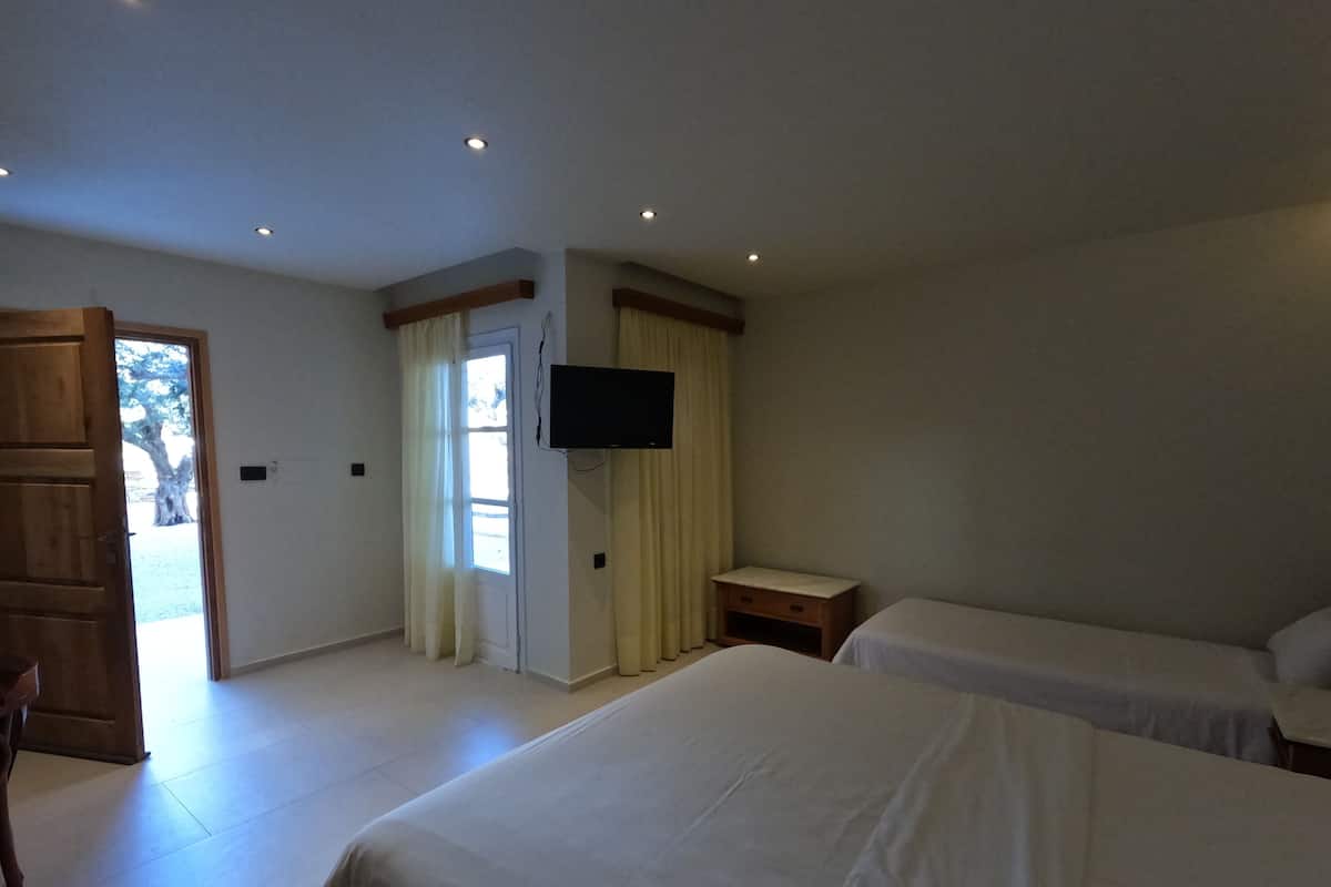 A hotel room with two beds, a TV, a wooden cabinet, and a door leading to an outdoor area.