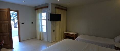 Habitación de hotel con dos camas, televisor, mueble de madera y puerta que da a un espacio al aire libre.
