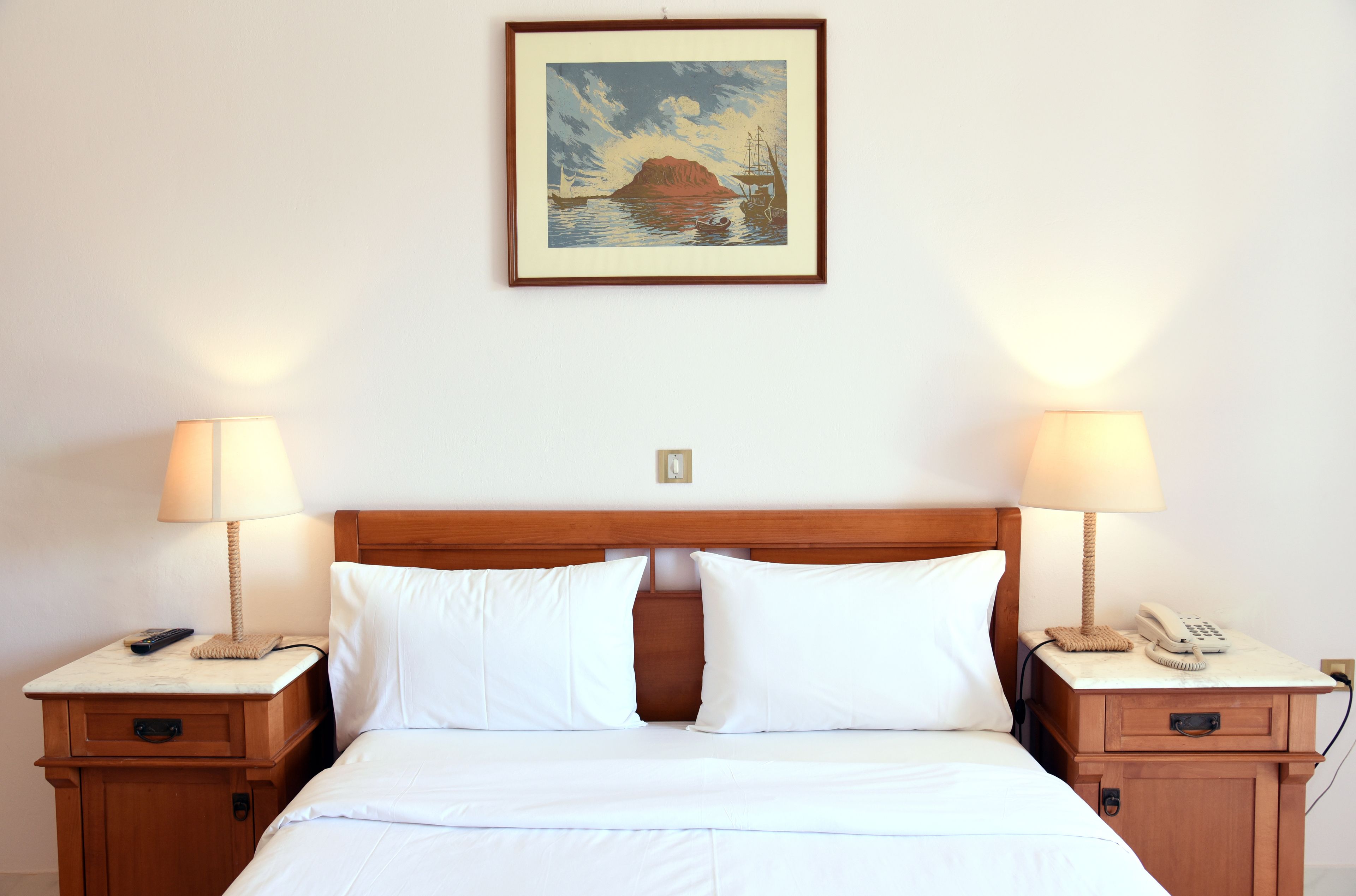 A hotel room with a bed, two bedside tables, lamps, a painting, and a telephone.